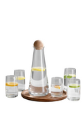 Clear carafe with wooden top on a marble surface with glasses containing water and lemon slices.