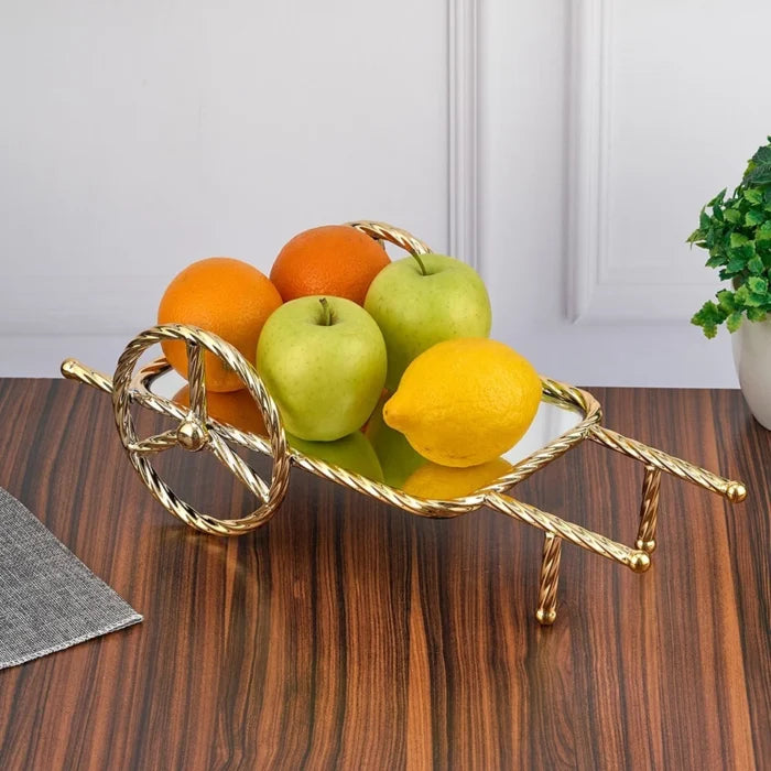 Decorative fruit bowl shaped like a wheelbarrow with fruits on a wooden table.