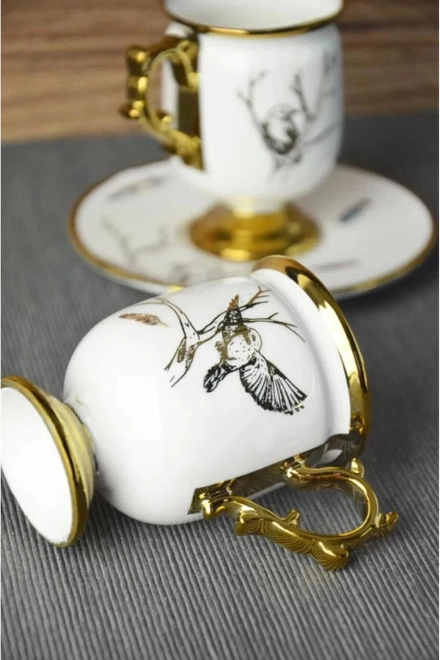 White ceramic teacup with gold accents and black floral design on a gray surface.