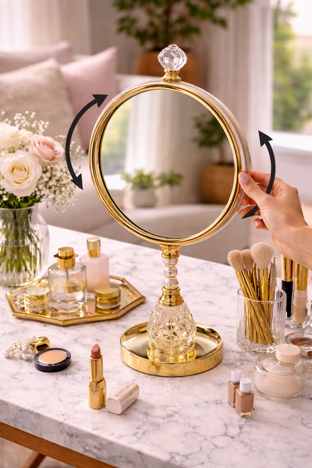 Gold vanity mirror with decorative stand on a marble surface with makeup items.